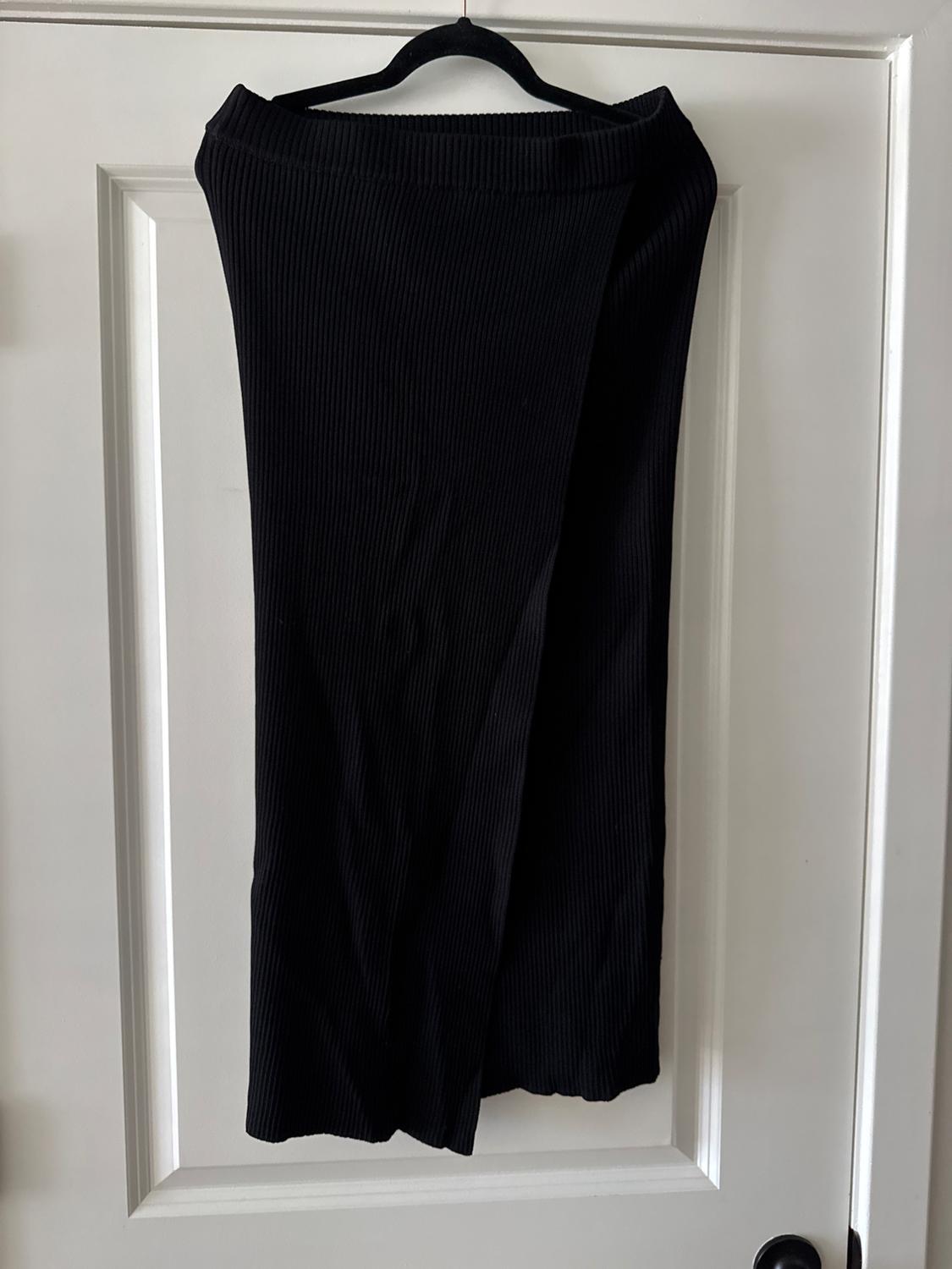 Black ribbed knit skirt hanging on a hanger over a white door.