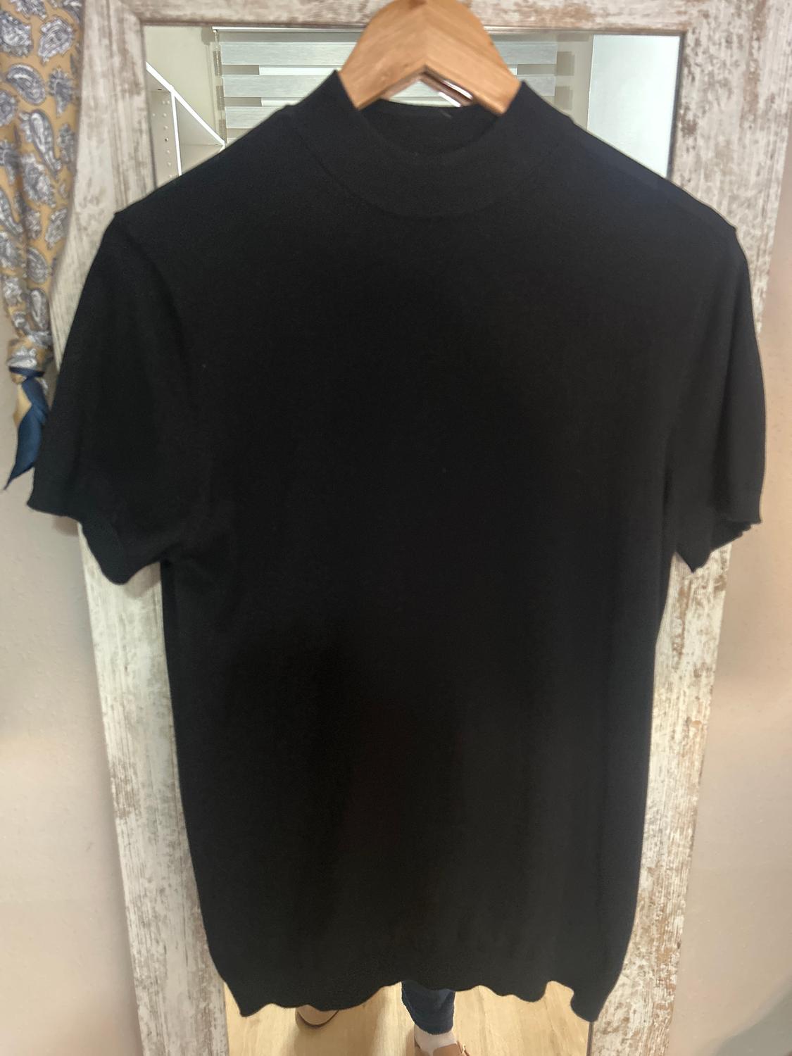 Black roll-neck top hanging on a wooden hanger in front of a distressed white-framed mirror.