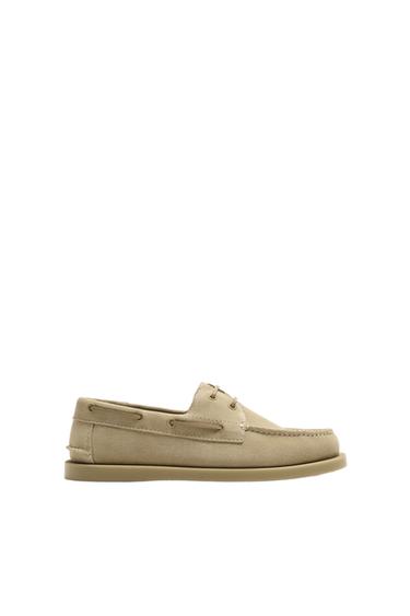 Side view of beige boat shoe with laces and flat sole.