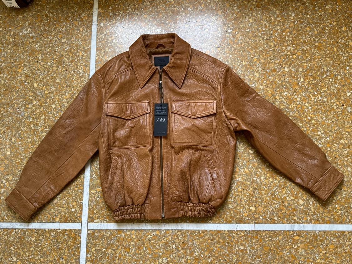 Brown jacket with zip fastening, collar, front pockets and elasticated hem on a terrazzo floor. Label bearing the text ZARA.