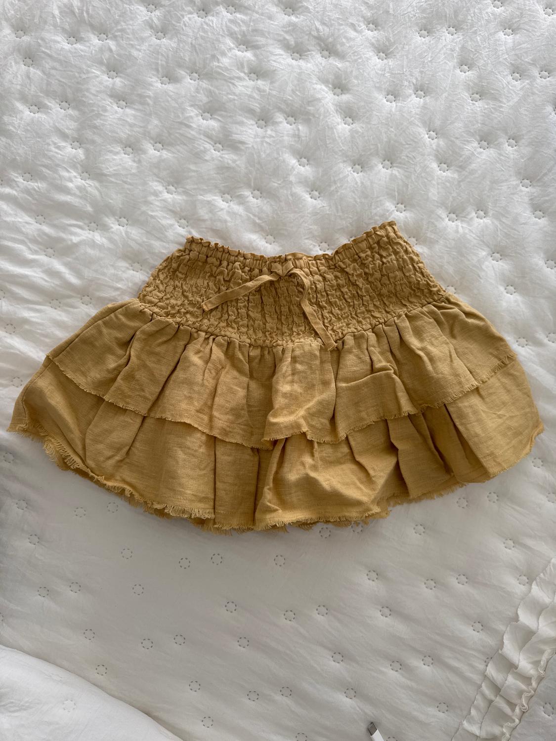 Short beige skirt with ruffles and an elasticated waist, on a quilted white bedspread with embroidered details.