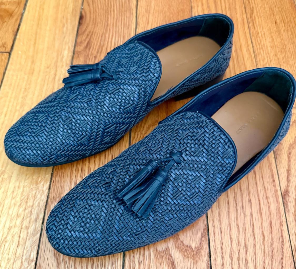 Blue wicker shoes with tassels, on a light wooden floor. Elegant and textured design.