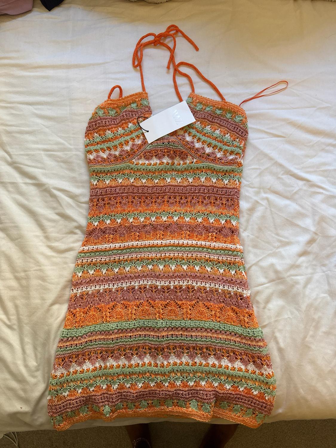 Short knit halterneck dress with an orange, green and white zigzag stripe pattern. ZARA label. Lying on a sheet.