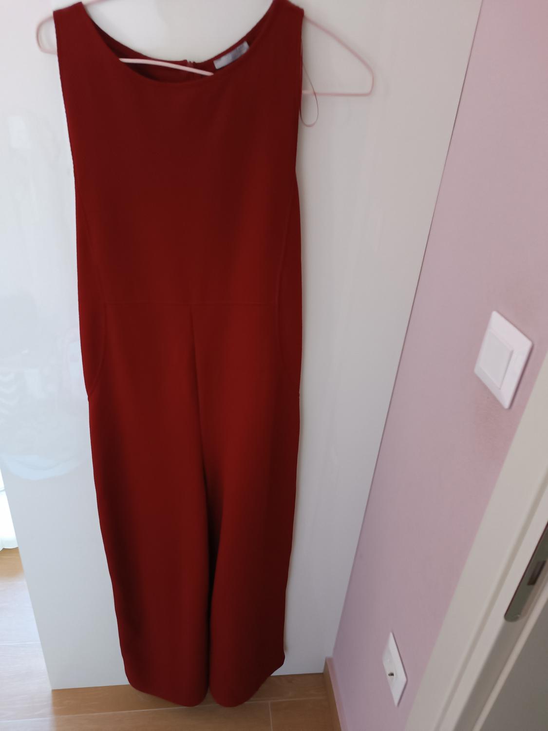 Sleeveless, long red dress hanging on a pink hanger over a white door. Pink wall background and light wooden floor.