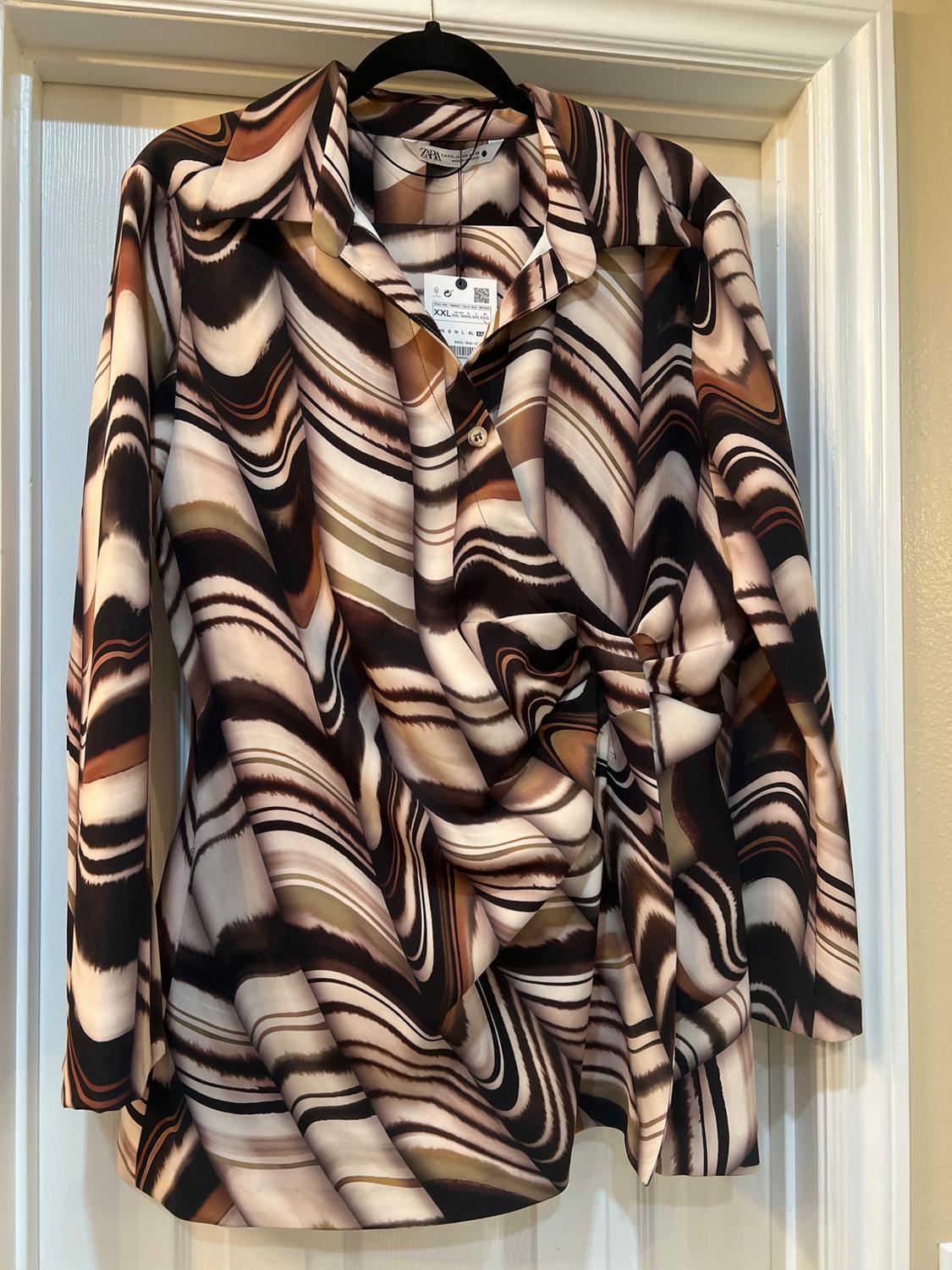 Long-sleeved shirt with an abstract print in shades of brown, beige, and black, hanging on a hanger over a white door.