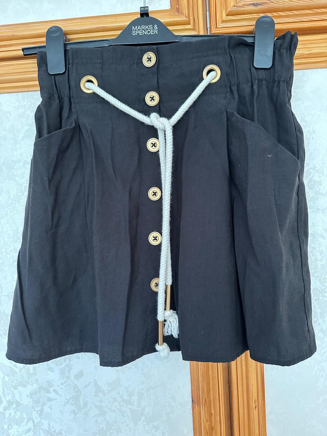 Front view of black skirt with gold buttons and cord belt. Visible side pockets.
