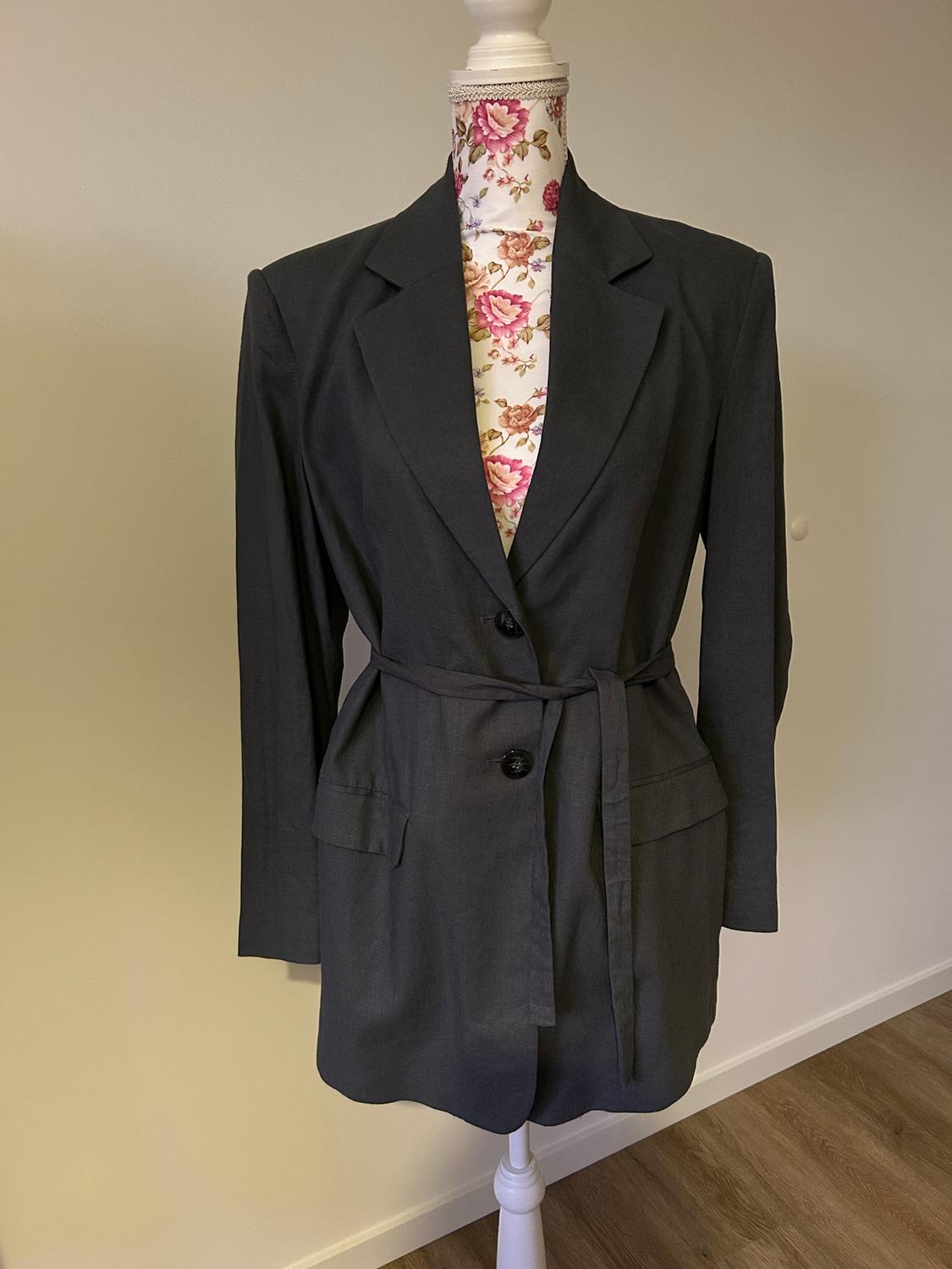 Mannequin with a dark grey button-up jacket and belt, on a neutral background. Mannequin's fabric with a pink floral print.