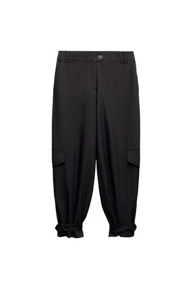 Black cargo-style trousers with side flap pockets and adjustable buttoned hems, presented on a white background.