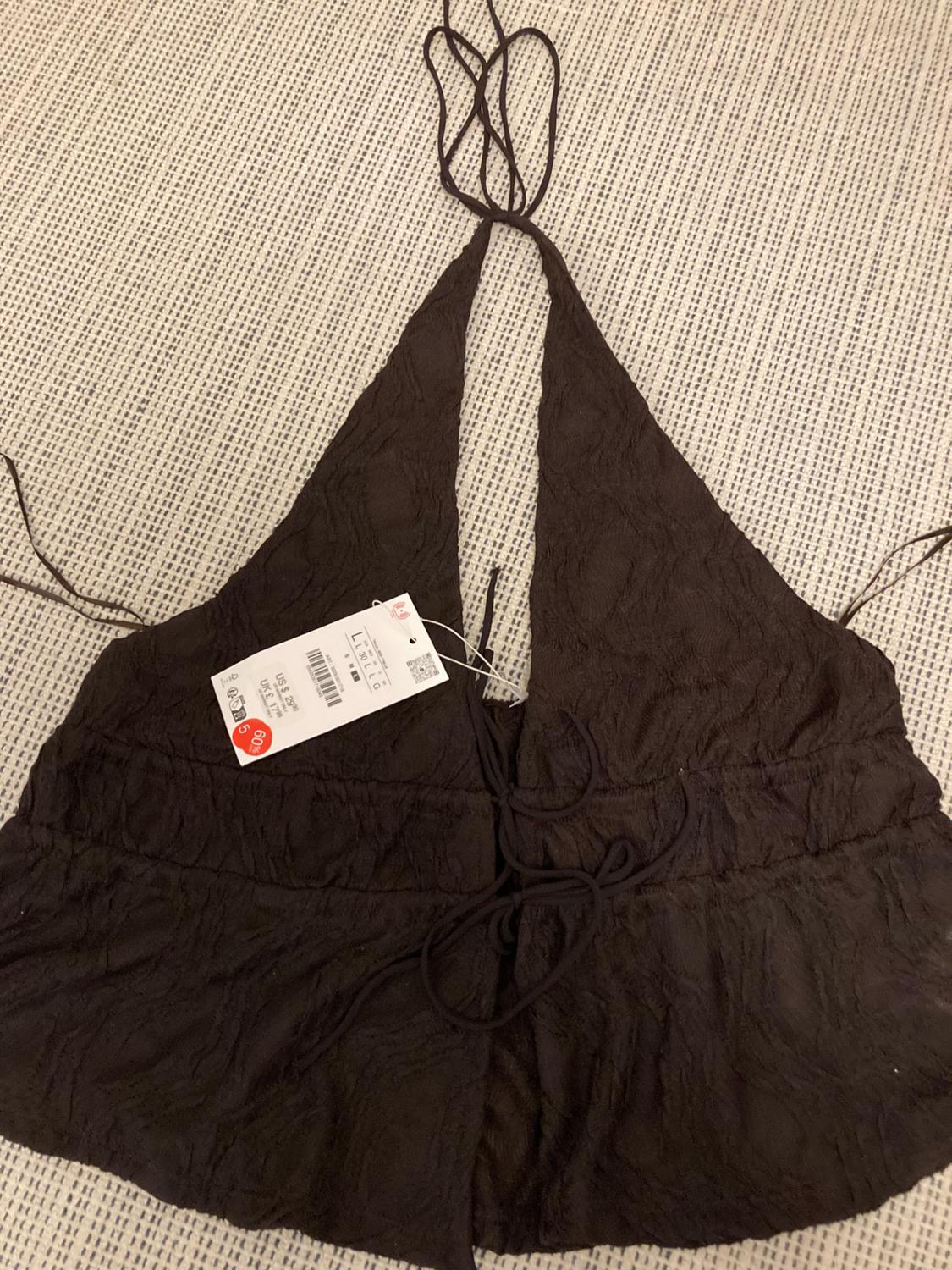 Dark brown top with thin straps on textured fabric. White tag with visible price and barcode. Light-coloured fabric background.