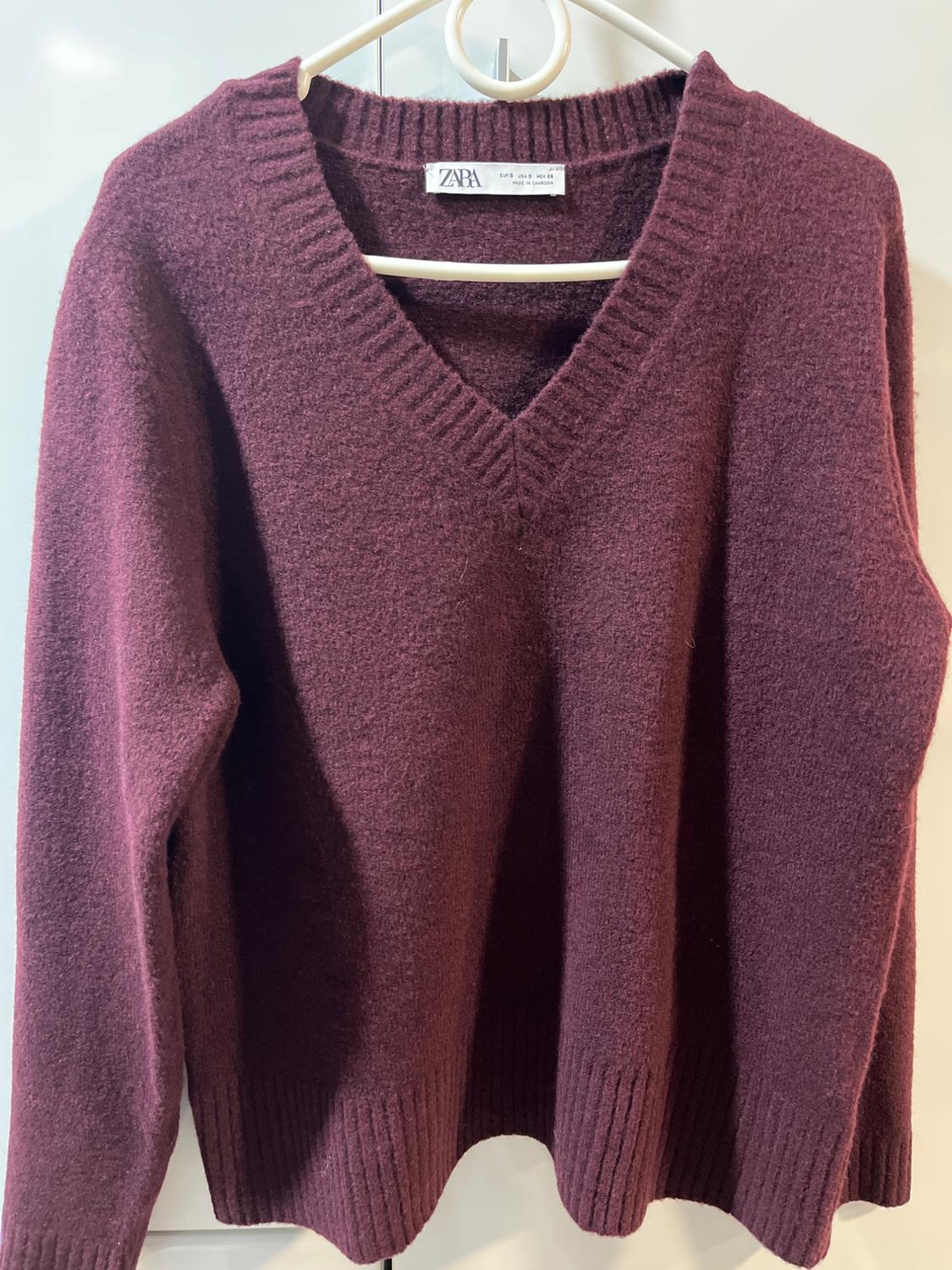 Burgundy chunky knit V-neck jumper, hanging on a white hanger. Visible label: "ZARA". White background.