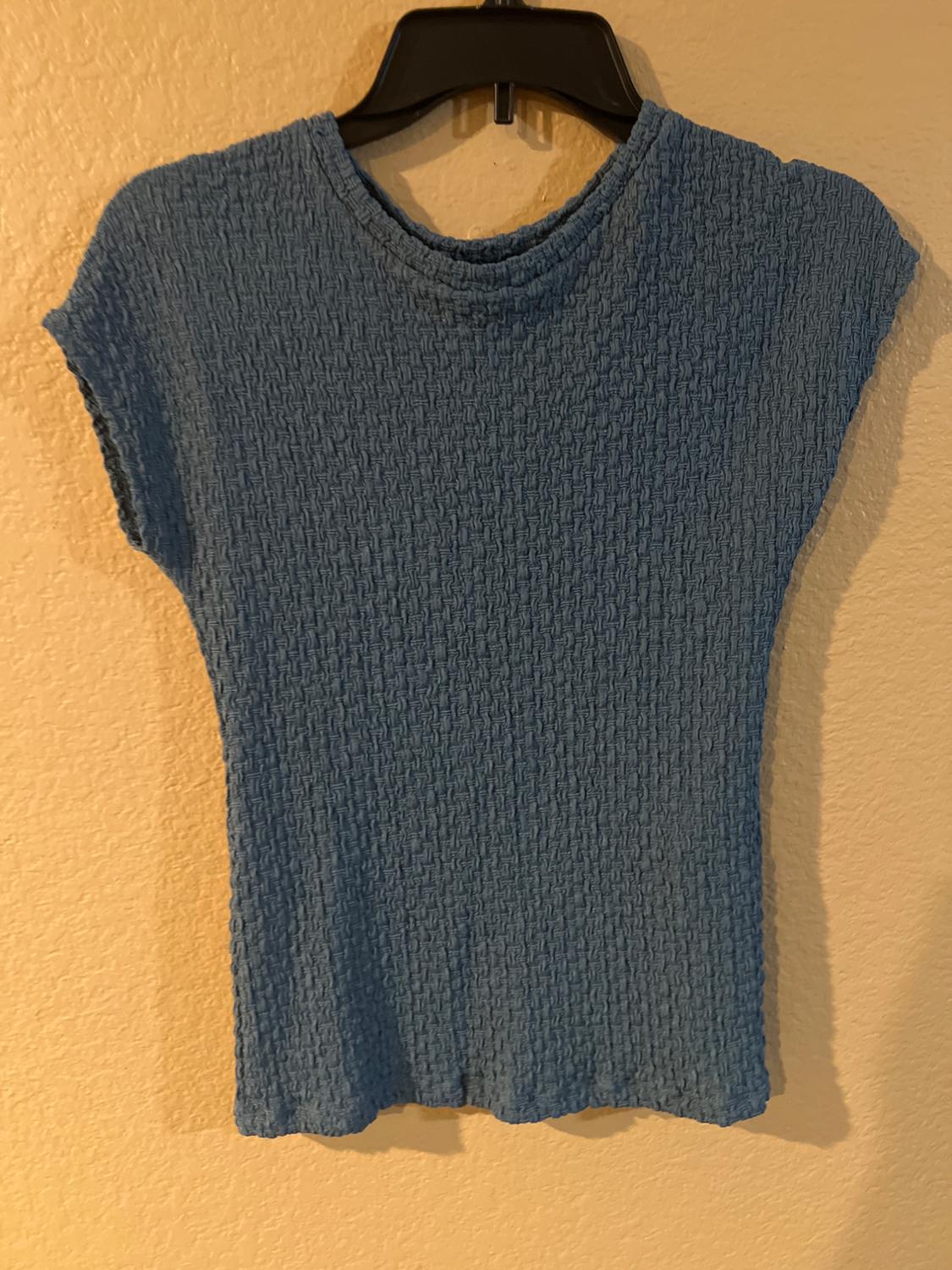 Blue crinkled-texture T-shirt hanging on a black hanger against a beige wall.