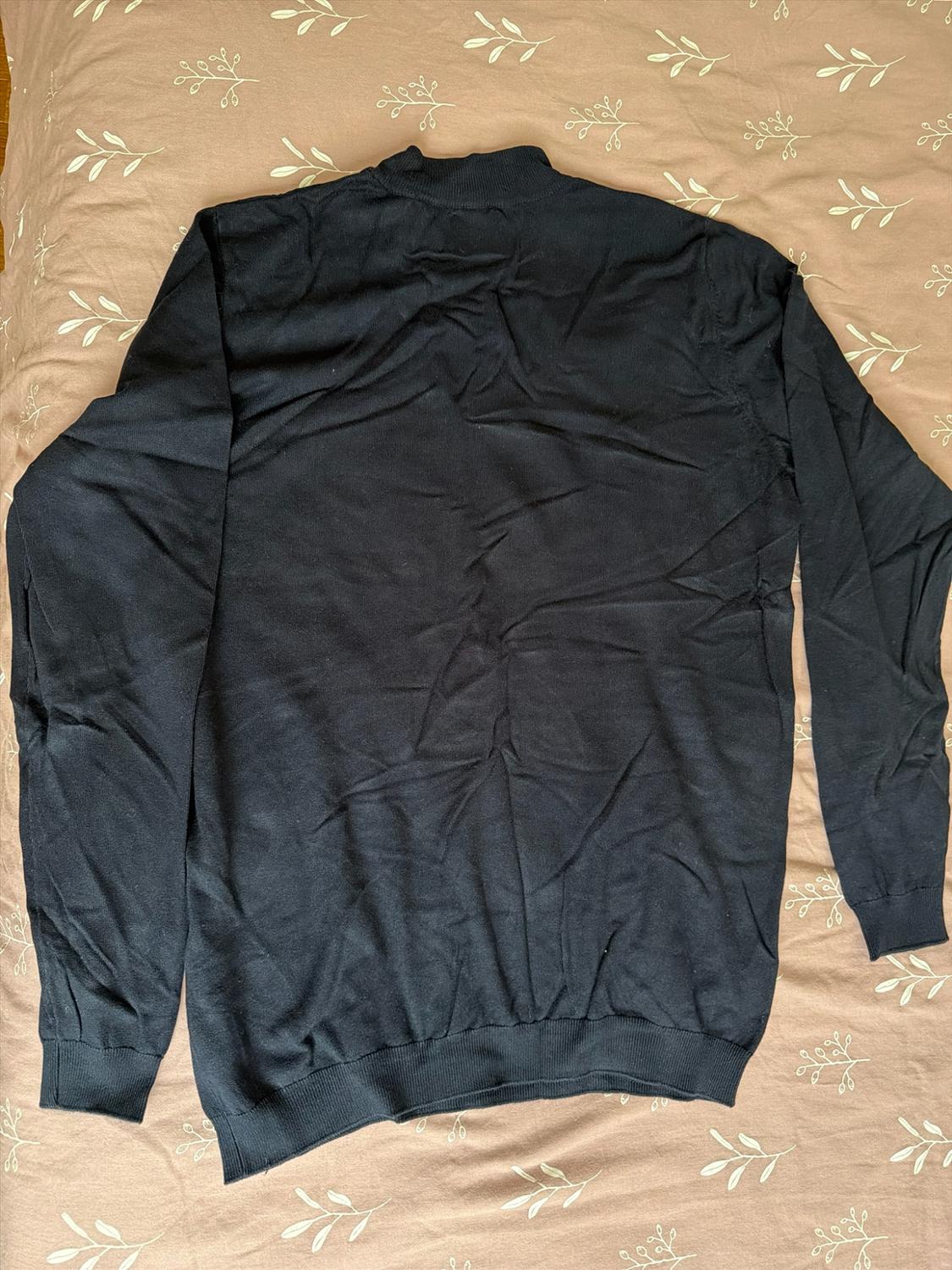 Long-sleeve crinkled black sweater with ribbed edges, laid out on a beige fabric with a leaf print.