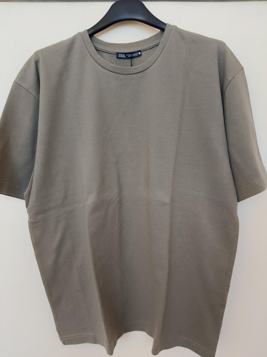 Olive green short-sleeved t-shirt hanging on a black hanger against a white background. The label reads ZARA.