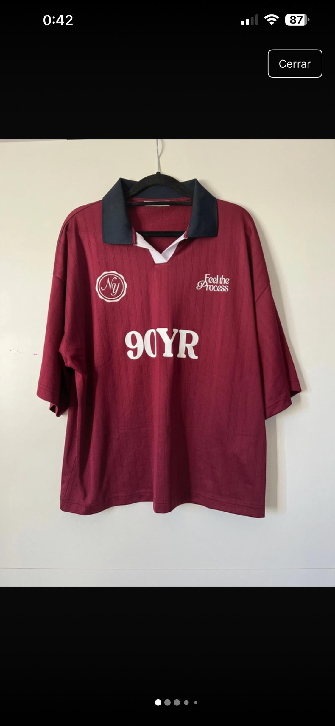 Burgundy T-shirt with navy blue collar, "Feel the Process" and "90YR" text in white, hanging on a black hanger.