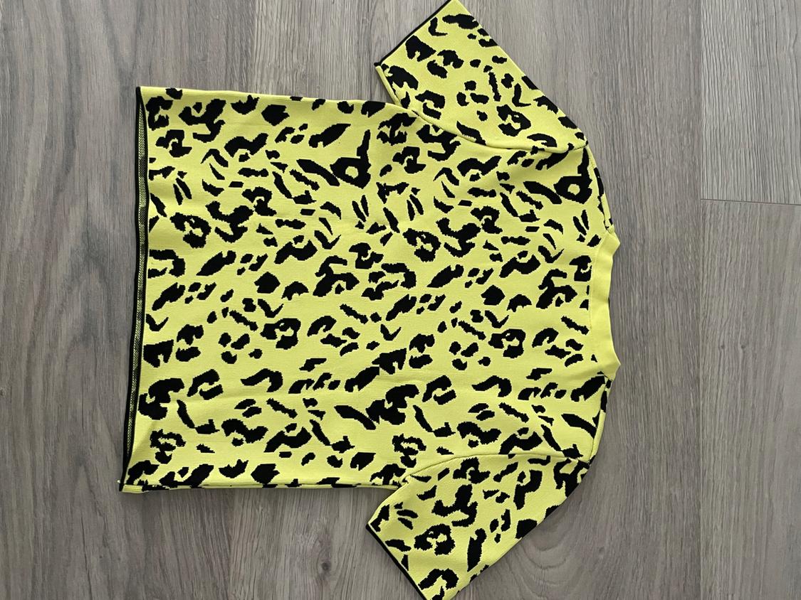 Yellow t-shirt with a black spot animal print design, on a gray wooden floor.
