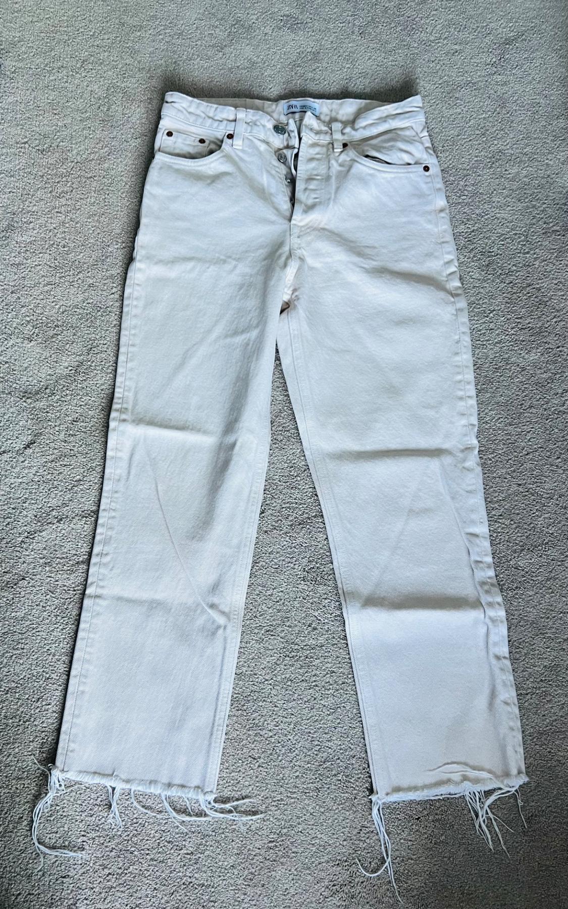 Front view of white pants with front pockets and frayed hems.
