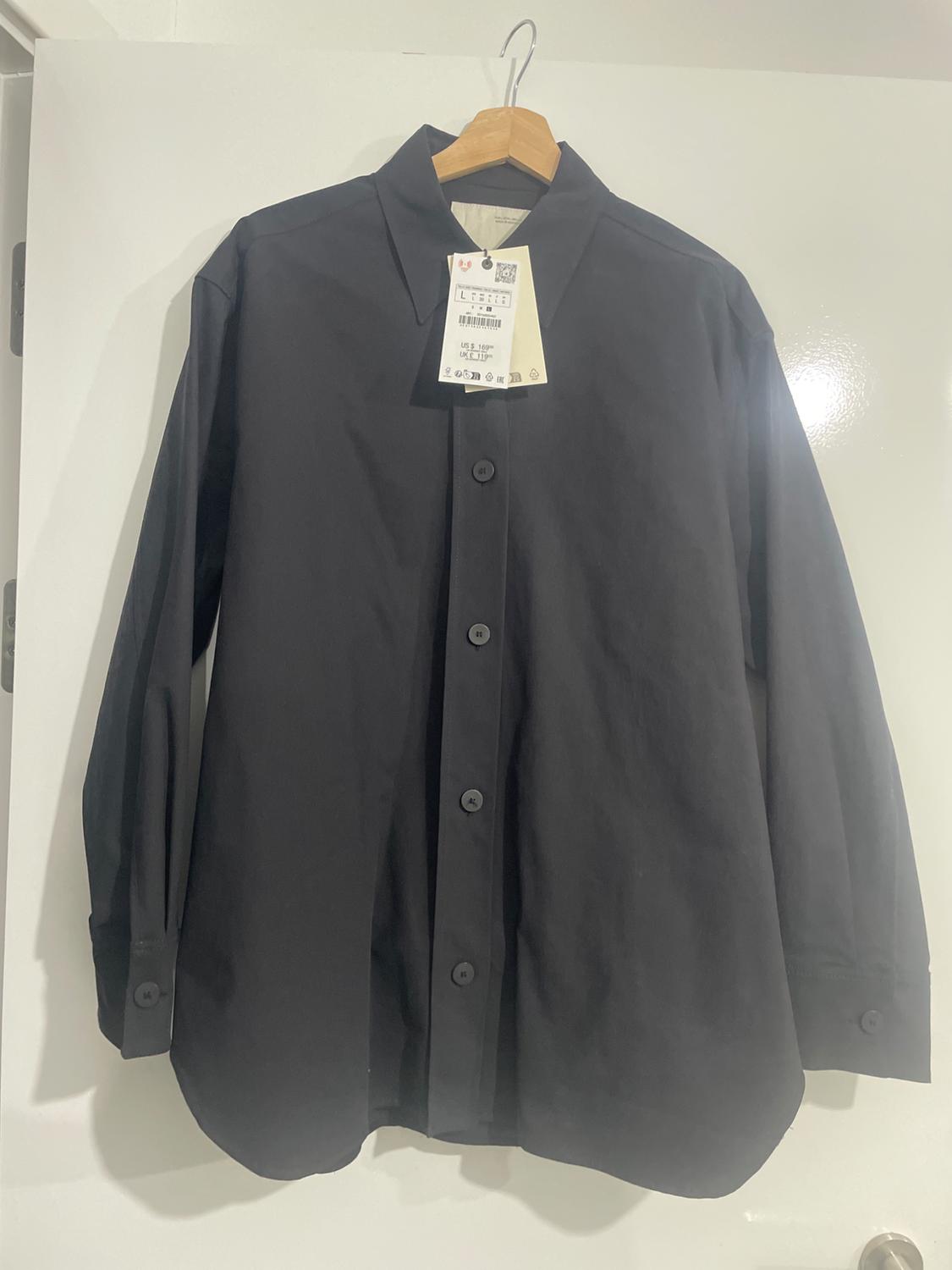 Black, long-sleeved shirt hanging on a wooden hanger, with a visible label showing size L and care details.