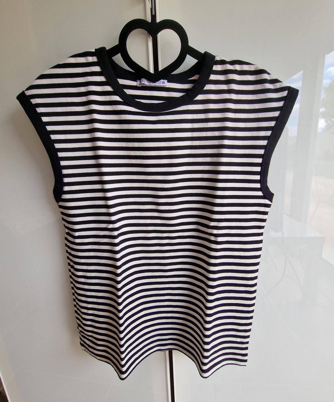 Black and white striped vest with black binding, on a black heart-shaped hanger against a white background.