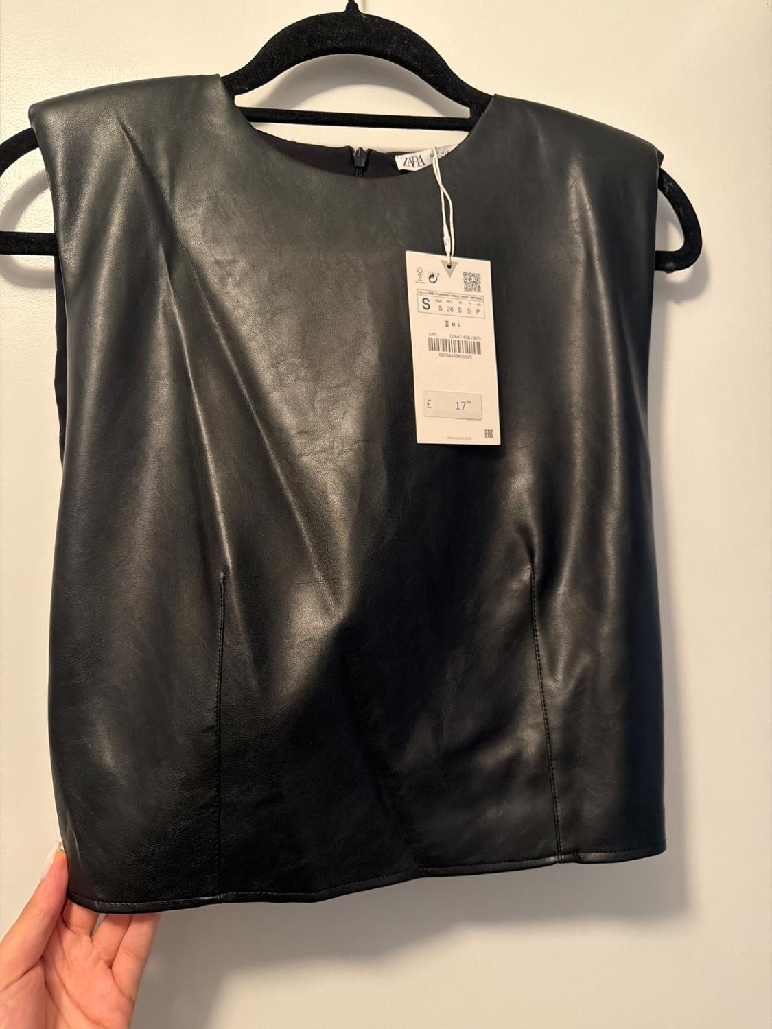 Black synthetic top hanging on a black hanger. Visible tag with price of £17 and size S. White background.