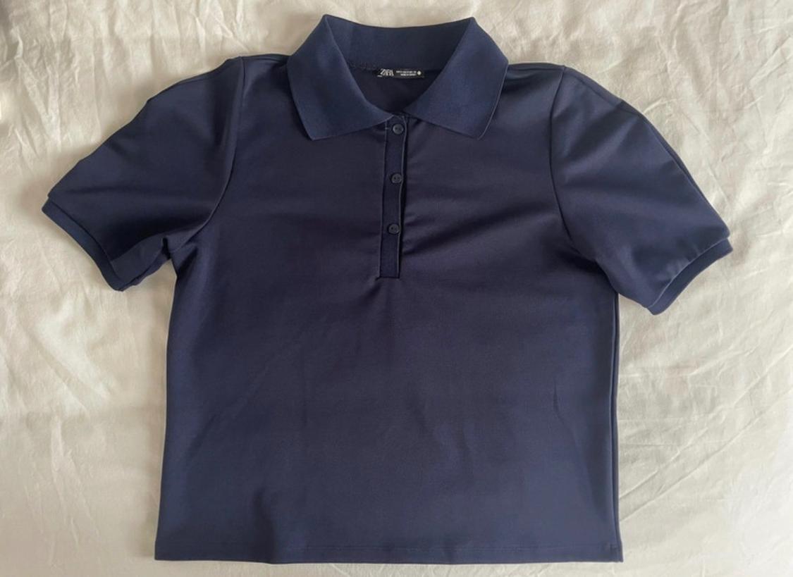 Navy-blue short-sleeved polo shirt with a classic collar and three buttons, laid out on a crumpled white cloth.