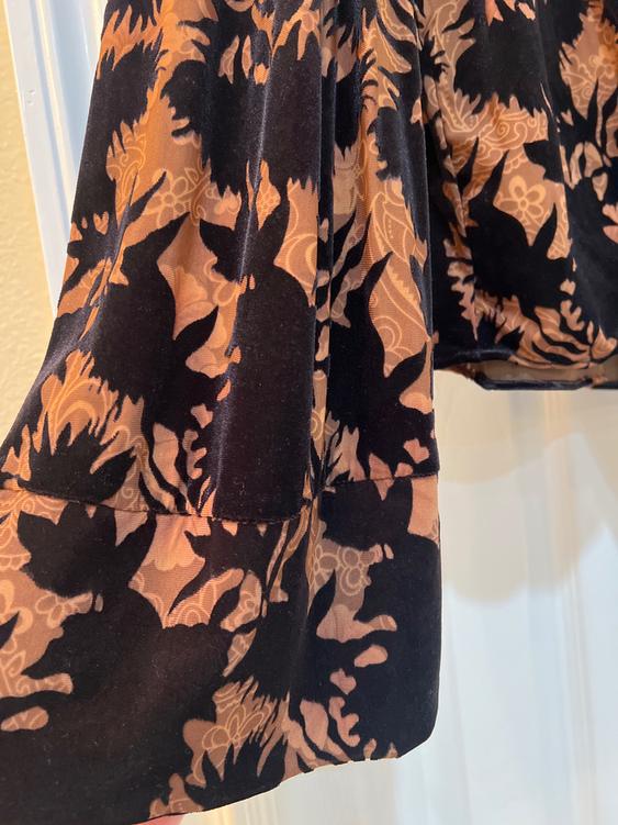 Fabric with a floral print in black and brown tones, with flower and leaf details, hanging over a light background.