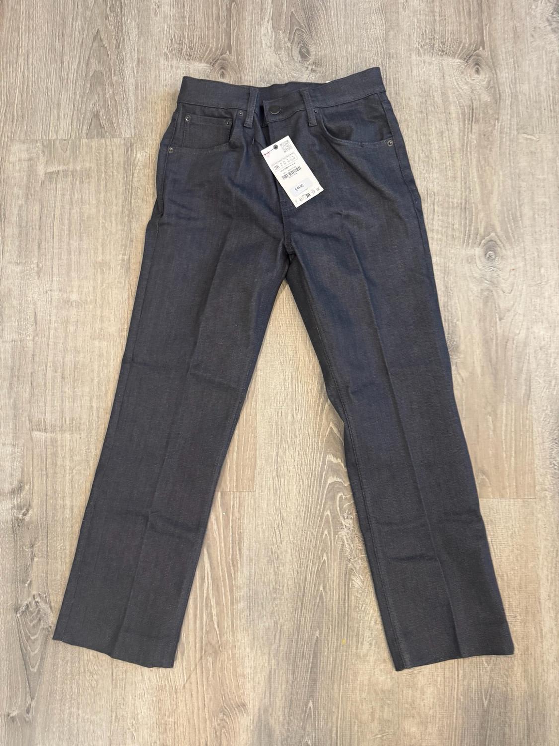 Dark straight-cut trousers with a label, laid out on a light wooden floor.