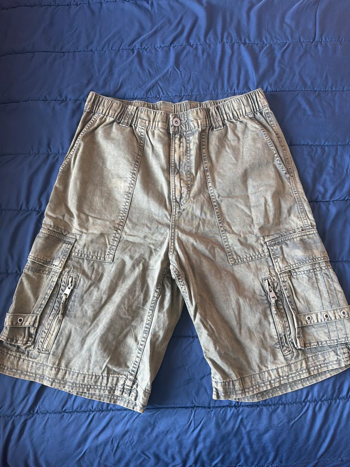 Grey cargo shorts with pockets and zips, on a blue quilted bedspread.