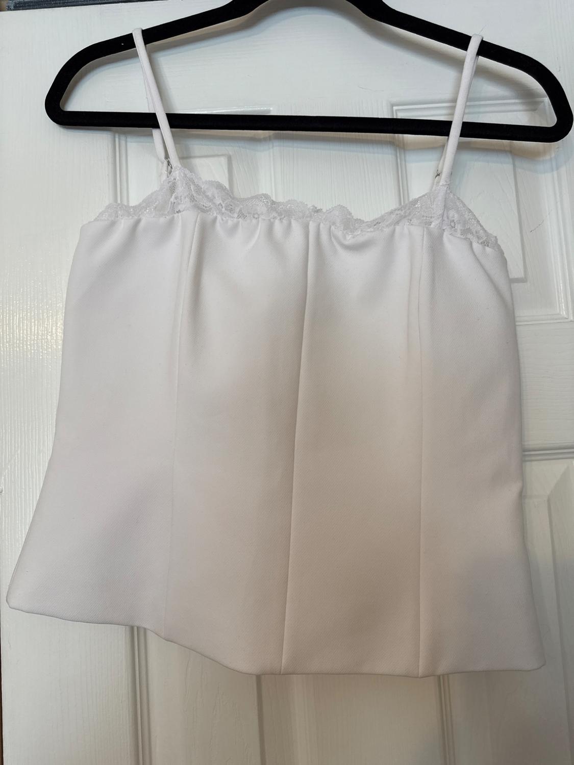 White spaghetti strap top with lace trim on the upper edge, hanging on a black hanger over a white door.