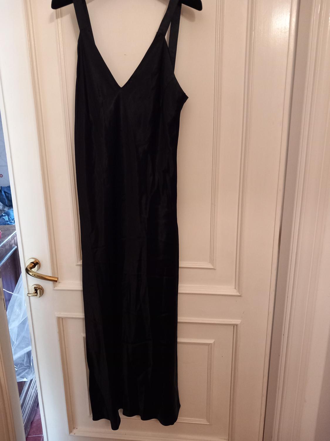 Black maxi dress with a V-neckline hanging on a hanger on a white door. Casual style in a homely and relaxed setting.