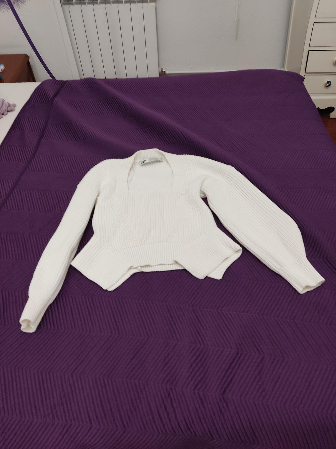 White knitted square-neck long-sleeve jumper, placed on a purple quilt on a bed.