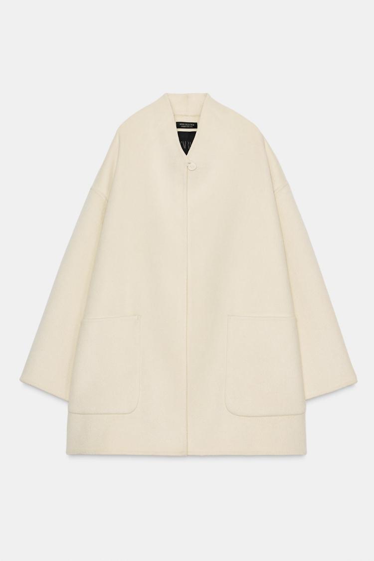 Sprednji pogled na kratek neobdelan plašč z ovratnikom, dolgimi rokavi in našitimi žepi. Zapenjanje spredaj z gumbom.