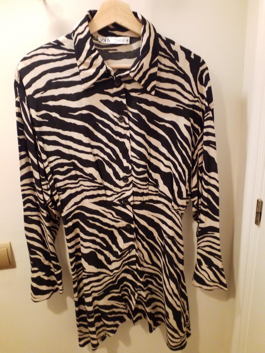 Long-sleeved shirt with black and beige stripe print, hanging on a wooden hanger against a white wall.