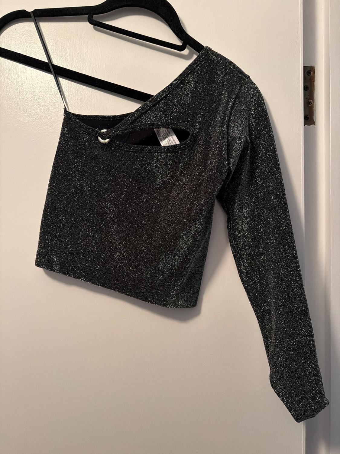 Shiny black one-shoulder top with a front cut-out, hanging on a black hanger over a white door.