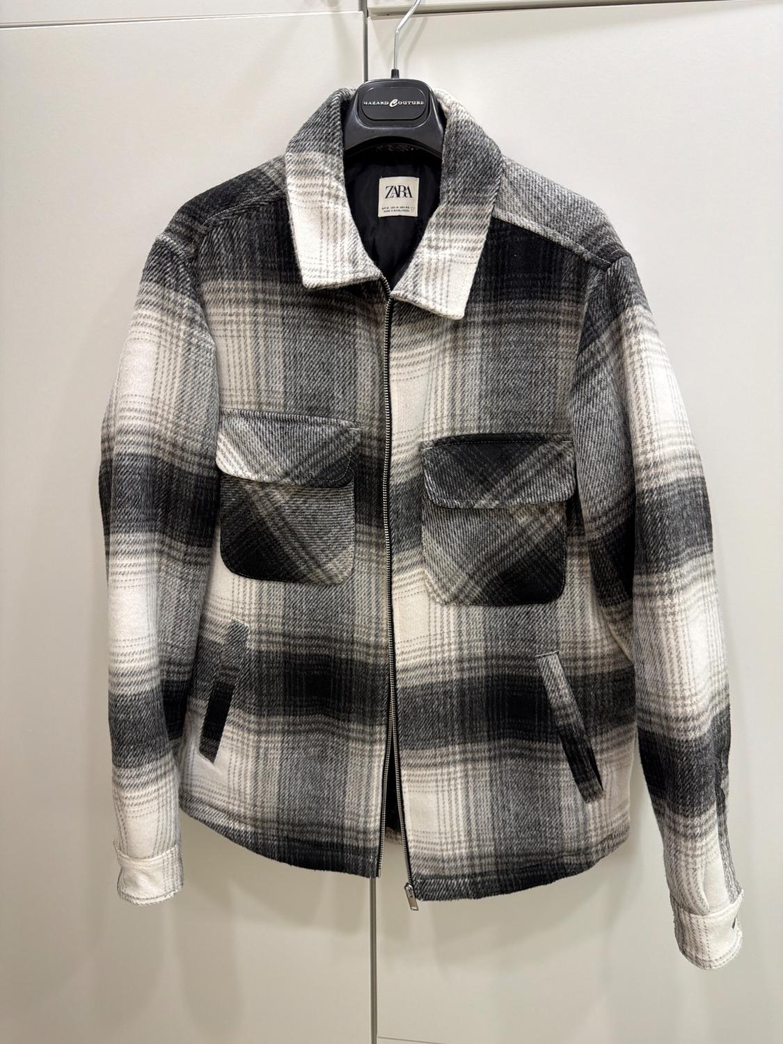 Black and white checked jacket hanging on a hanger. Visible label with the text "ZARA". Large front pockets.