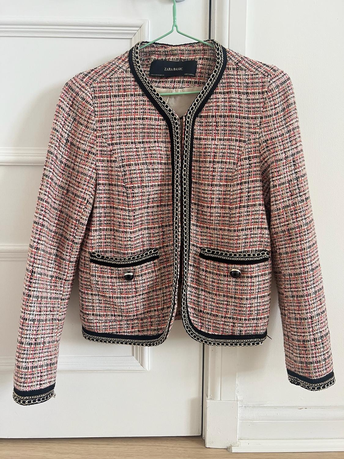Pink, black and white textured jacket with piping and silver chain, hanging on a white door. Label: ZARA BASIC.