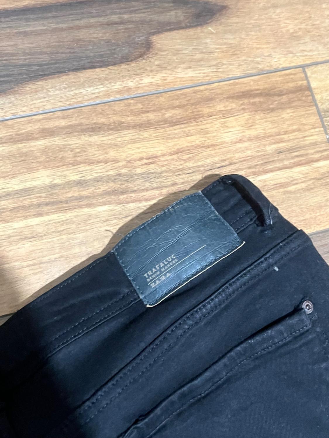 Label detail on the back of black trousers, text 'TRAFALUC DENIM ZARA'.