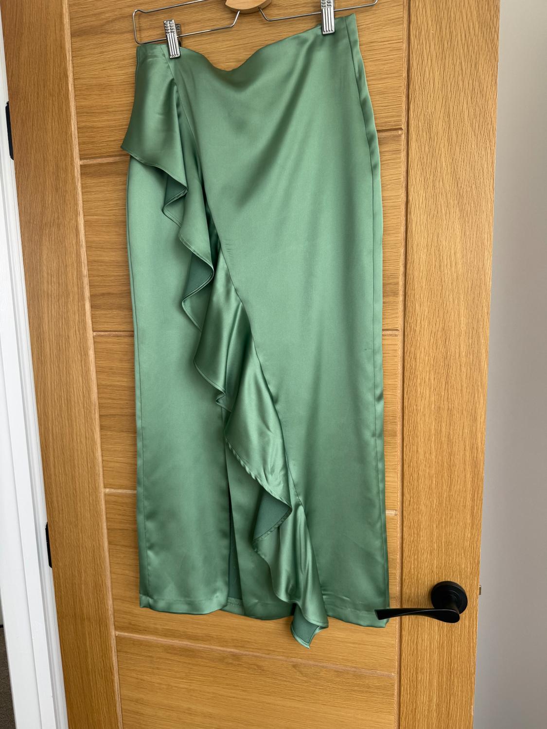 Satin green ruffled skirt hanging on a light wooden door.