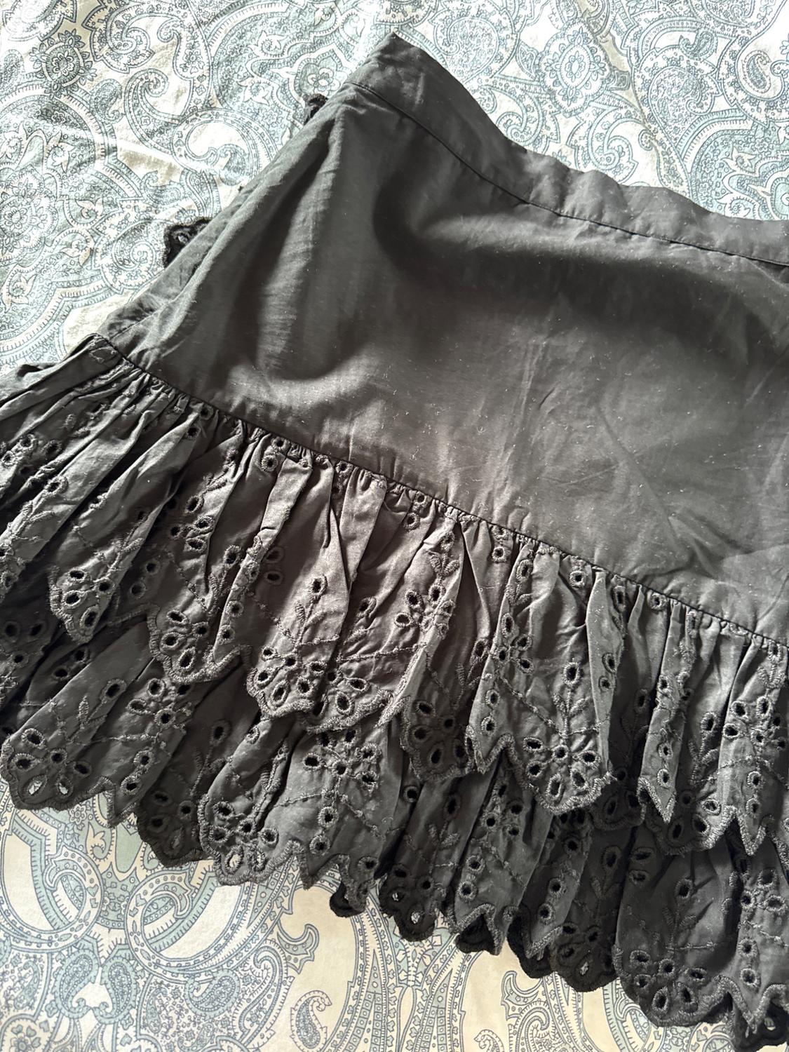 Black skirt with ruffles and openwork embroidery on the hem, over a paisley print fabric in blue and white tones.