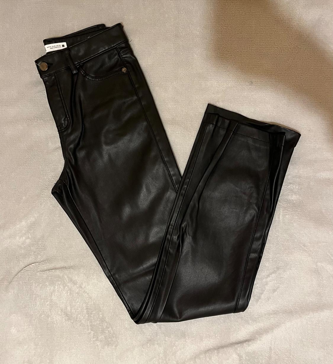 Black synthetic trousers, folded on a beige surface. Label visible at the waist.