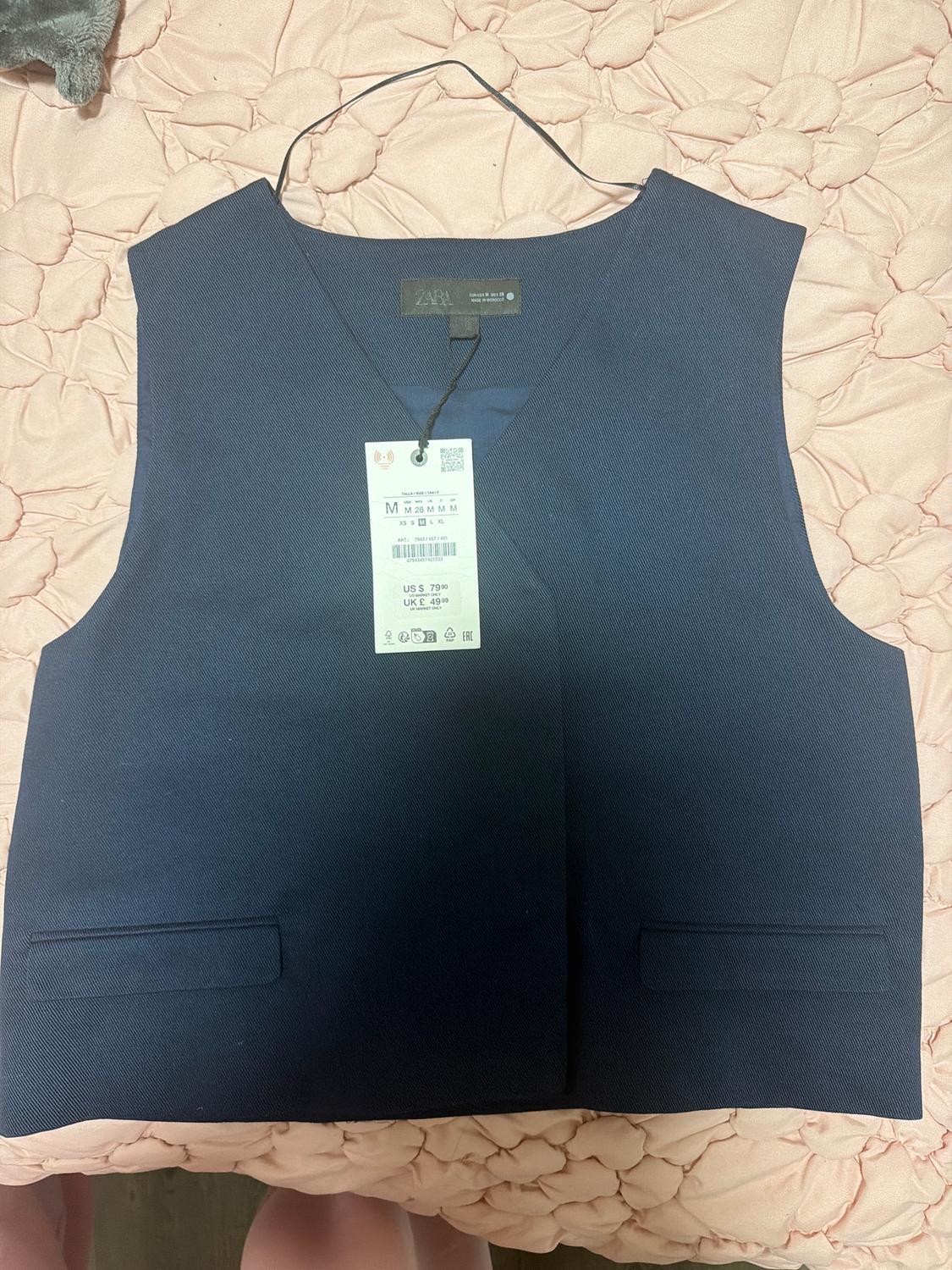 Navy blue vest on pink quilt with visible price tag. Tag shows sizes M, US S, UK E 40/90.