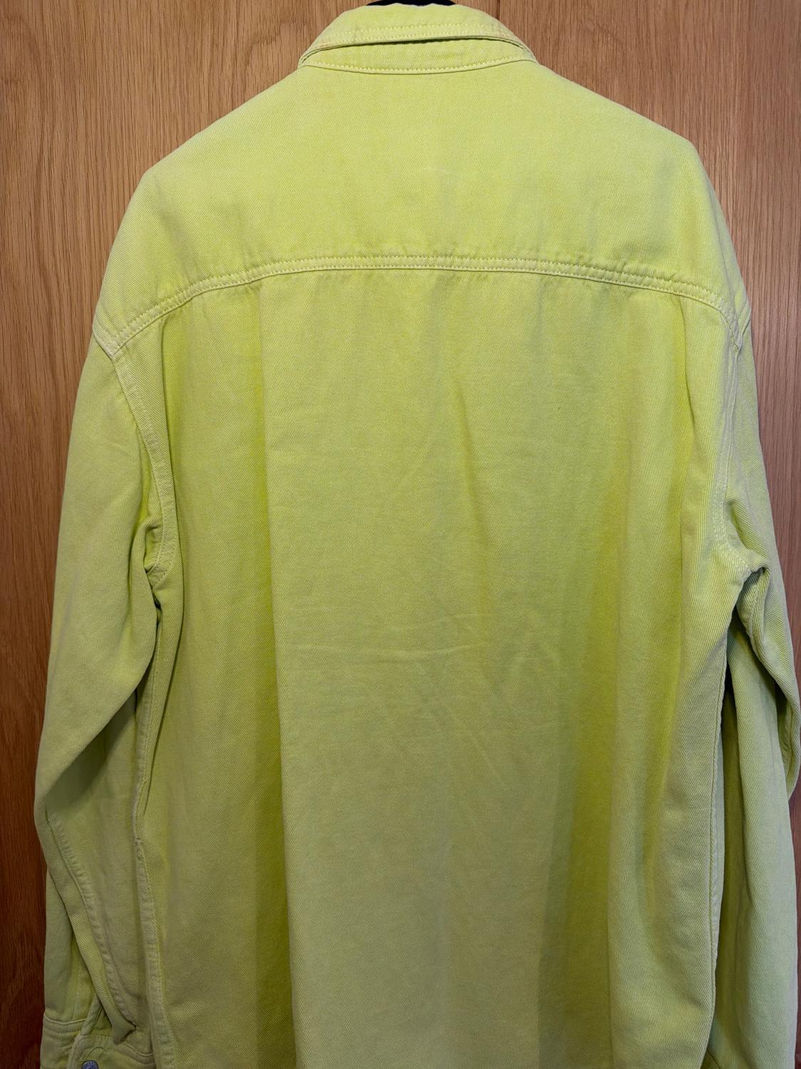 Lime green shirt viewed from behind, hanging against a light wooden background.