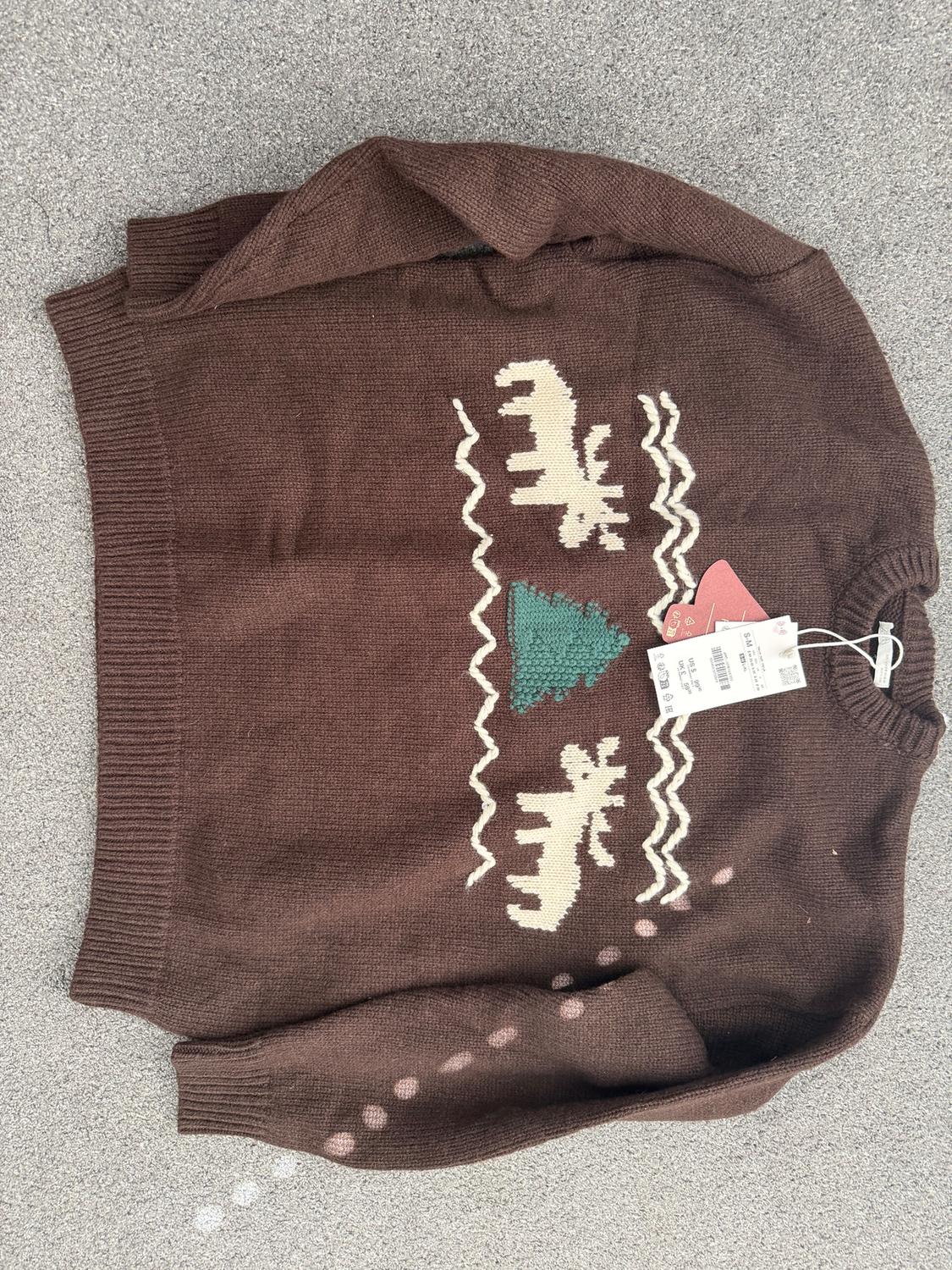 Brown jumper with elk and green tree design, visible hang tags, on a grey background.