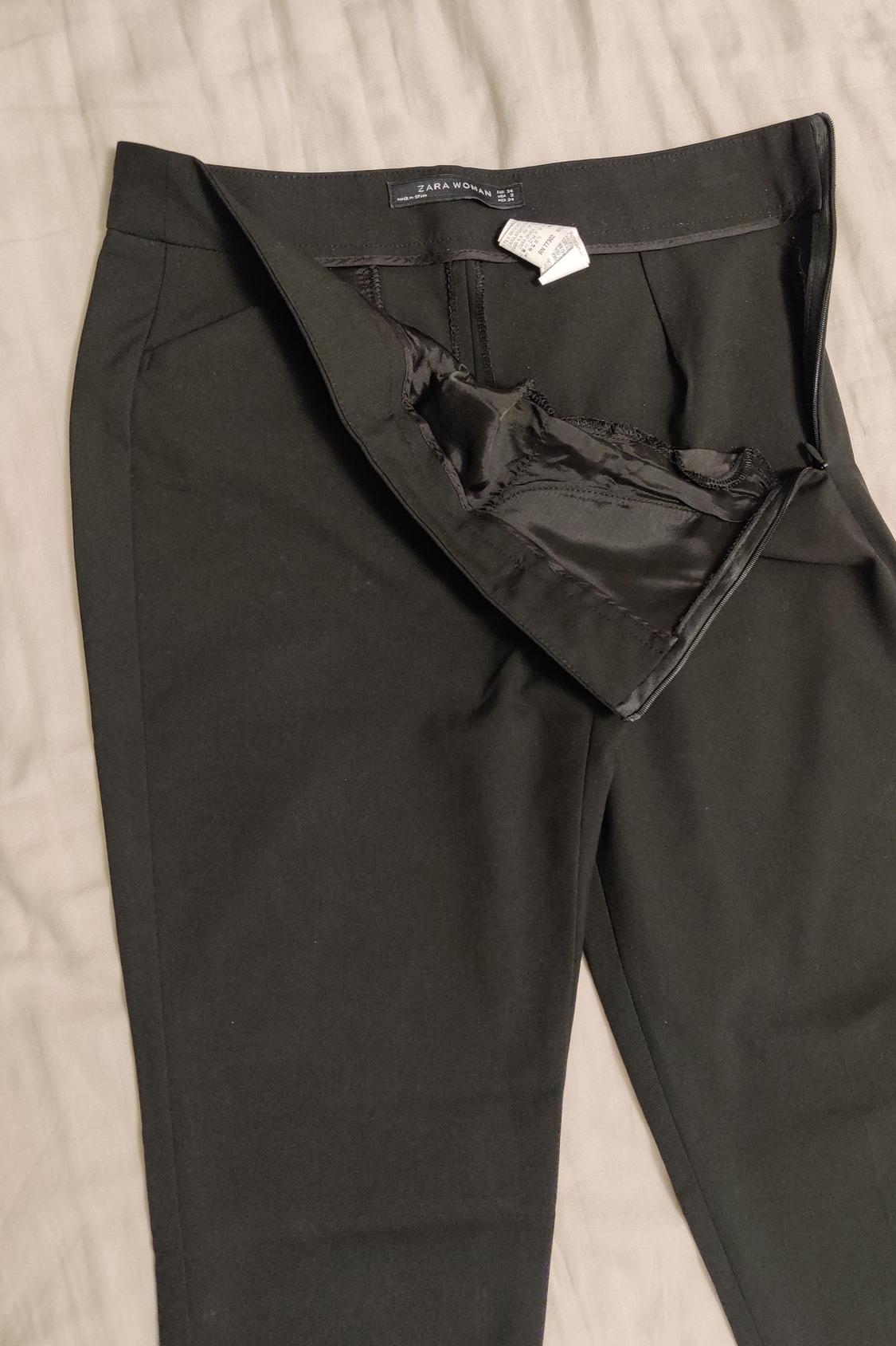 Detail of black trousers with open zip and visible label.