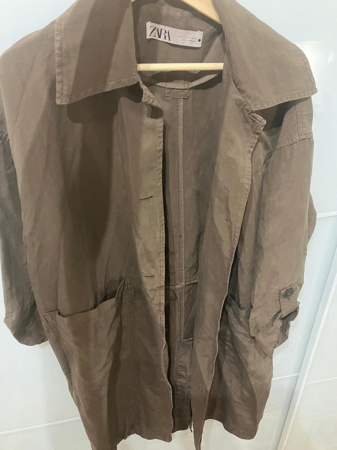 Brown coat hanging on a hanger, with large pockets and a visible Zara label on the inside of the collar.