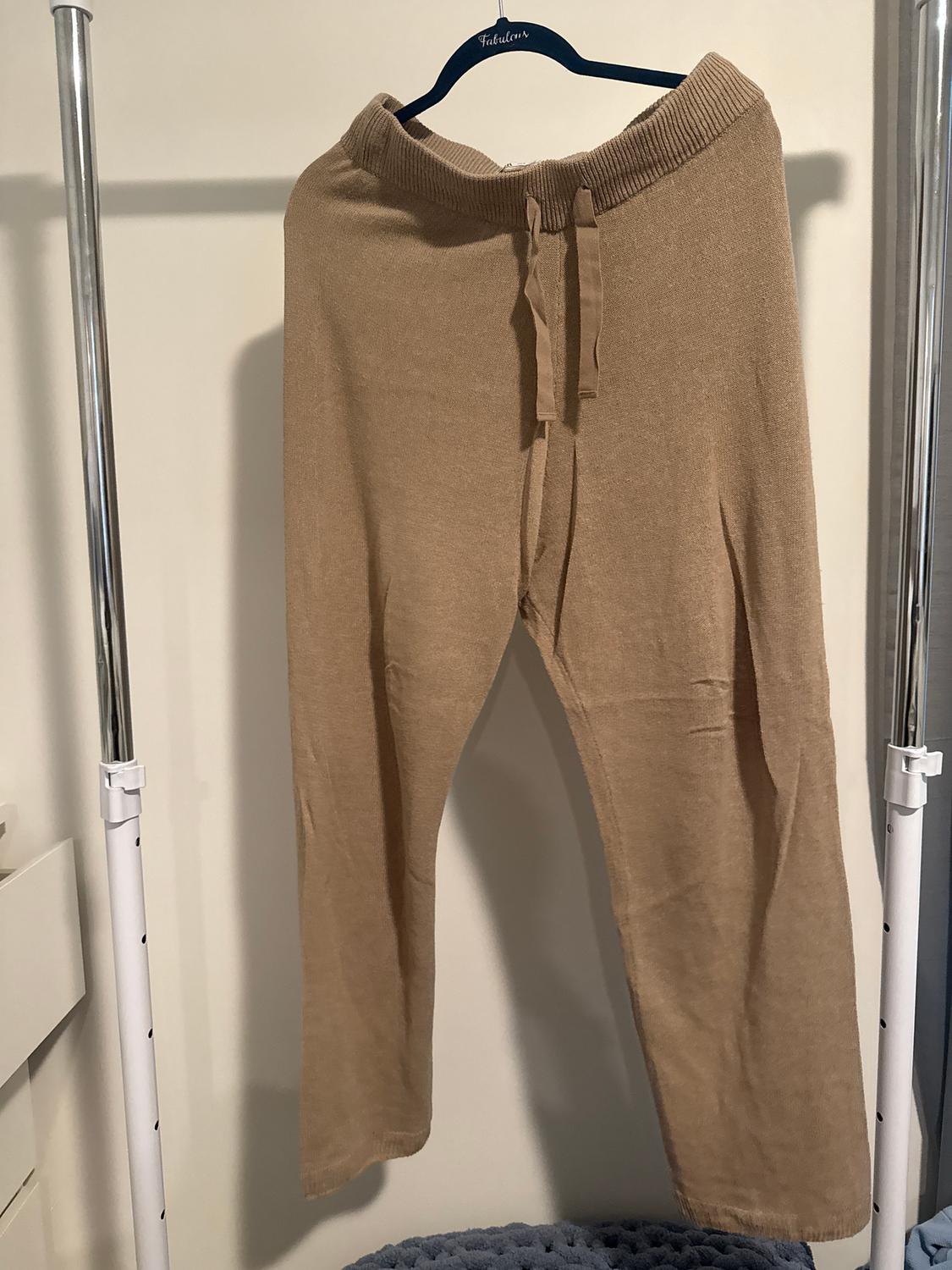 Beige trousers hanging on a black hanger with the brand "Fabulous", against a white background.