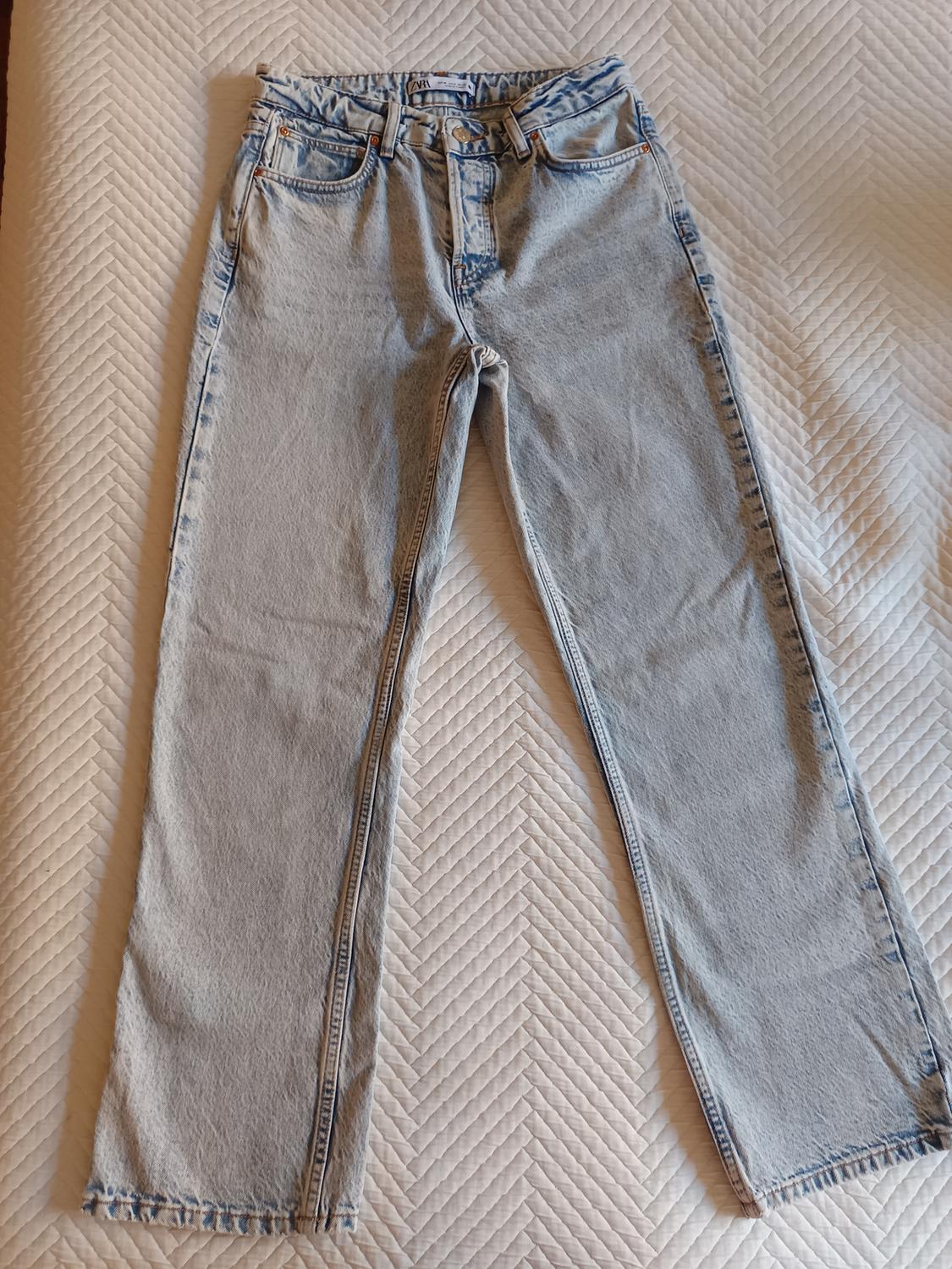 Light blue denim jeans with a straight cut, placed on a white herringbone patterned quilt.