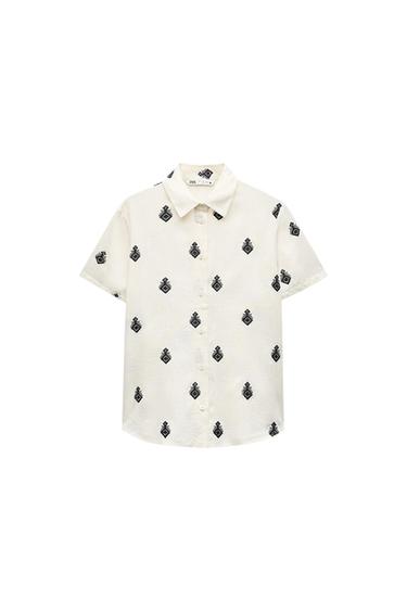Ecru short-sleeve shirt with black geometric patterns. Front button closure. Label on the collar with the text ZARA.