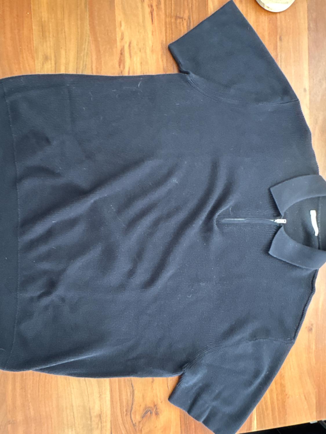 Black short-sleeved polo shirt with zip-up neck, on a wooden surface.
