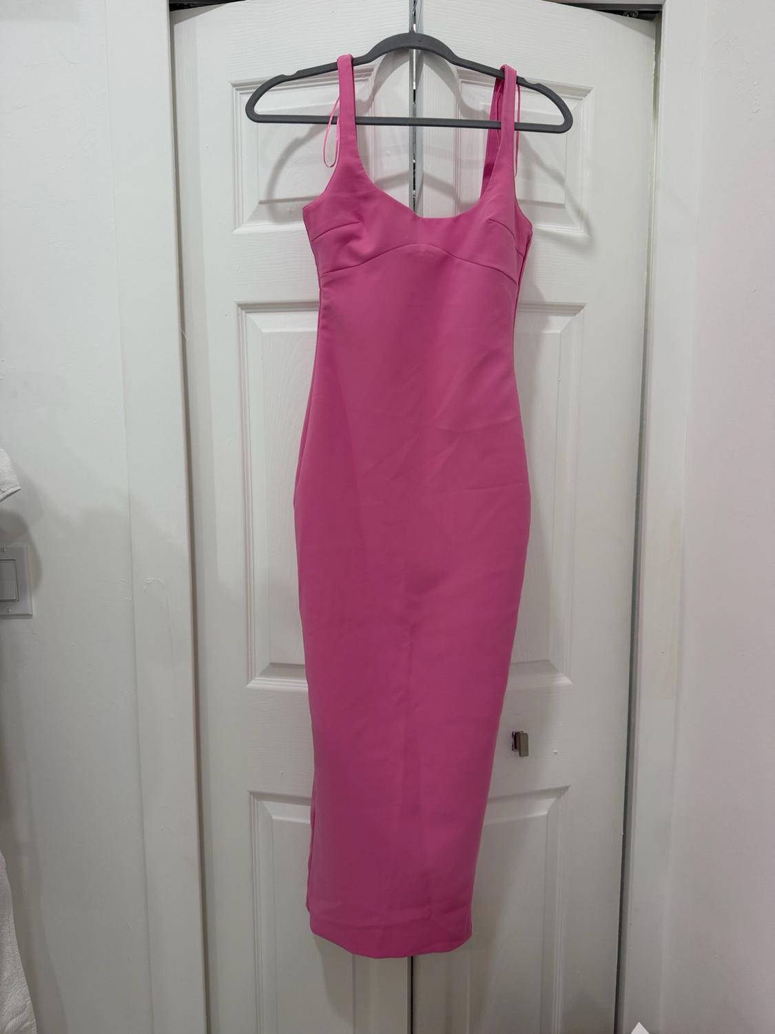 Fitted pink midi dress with wide straps hanging on a hanger over a white door.