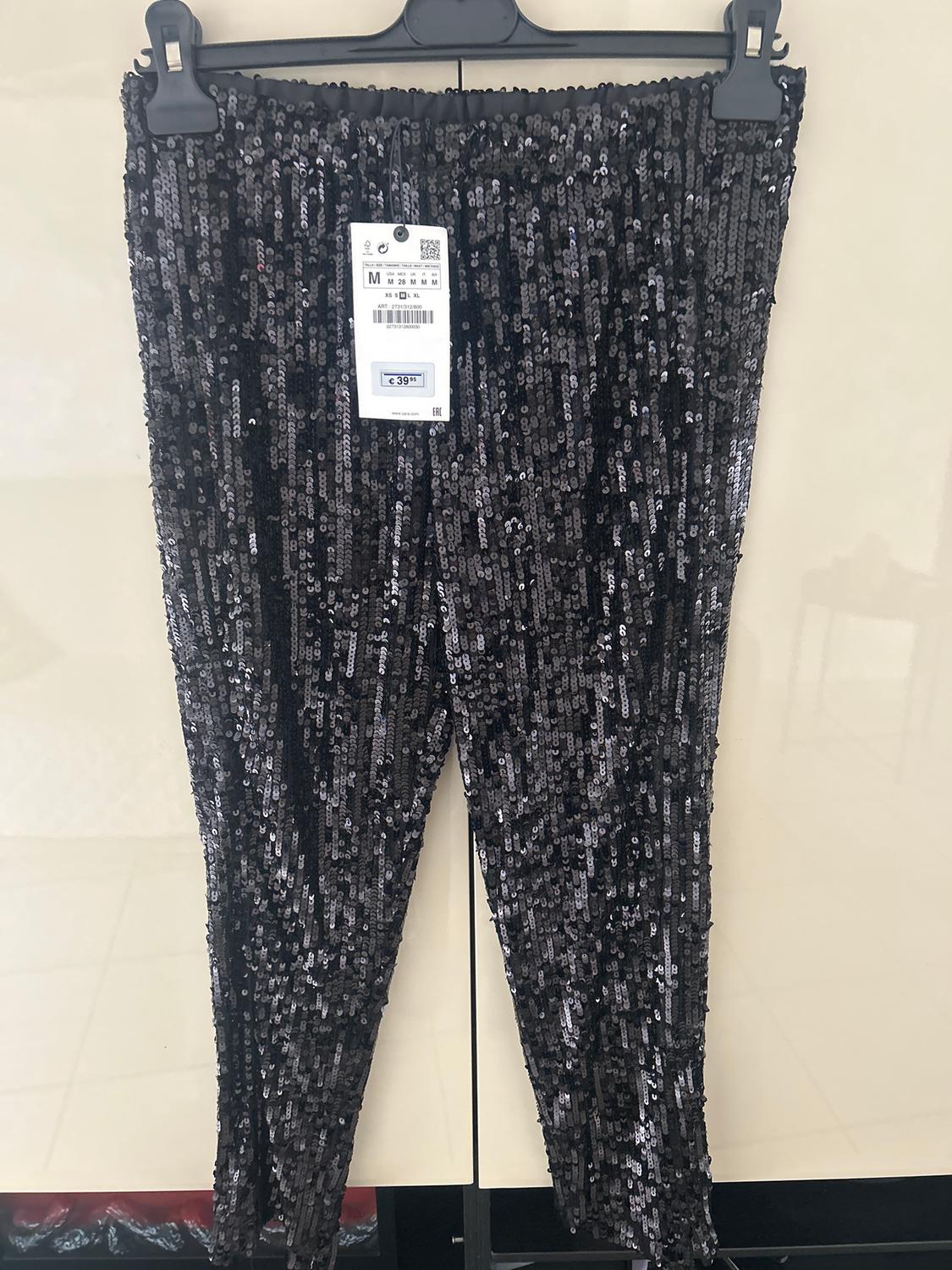 Black sequinned trousers hanging on a hanger, with a visible tag showing a price of €39.99. Light background.